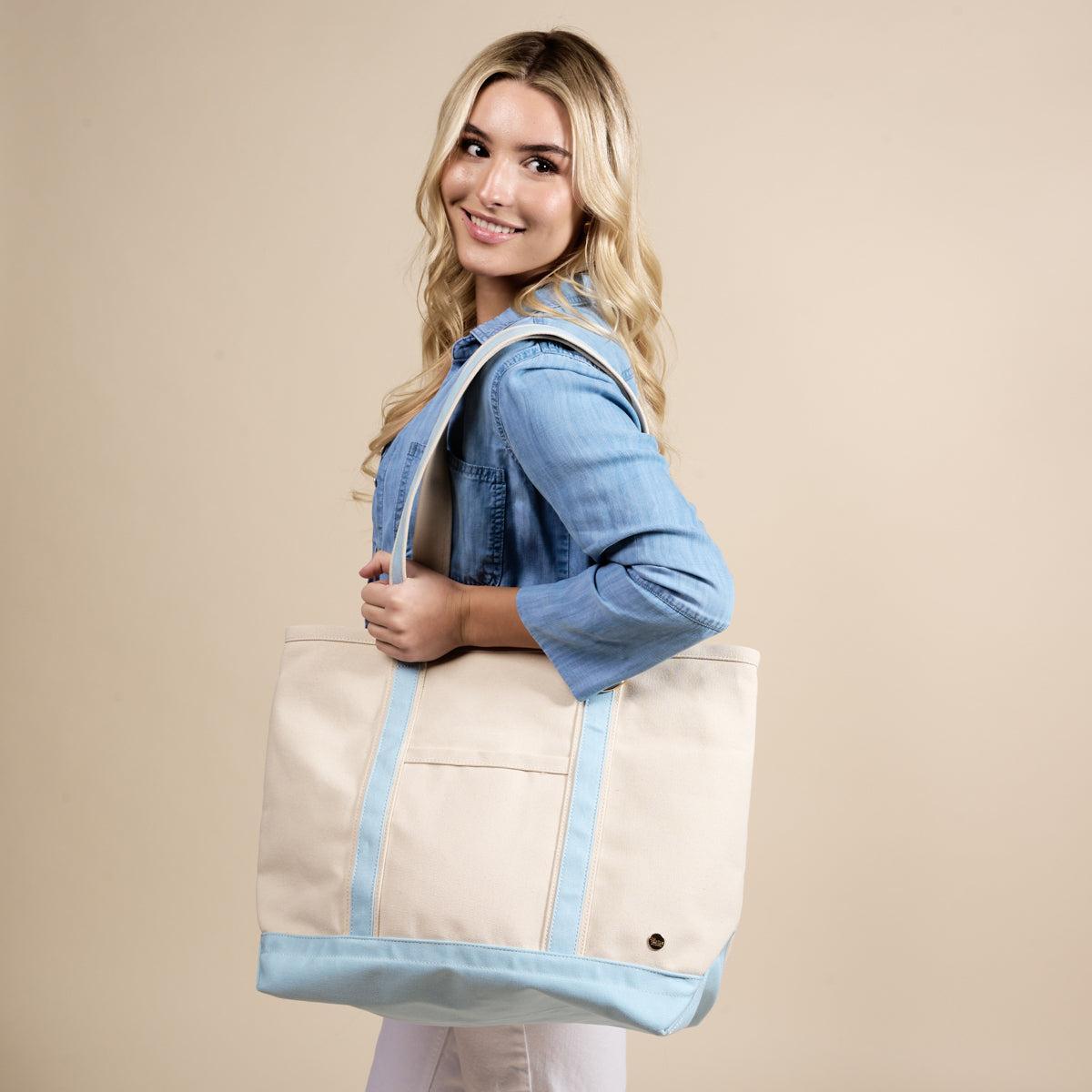 The Signature Canvas Tote Bag, A natural canvas tote bag with black webbing straps, a front pocket, and a gold D-ring, shown against a cream background.