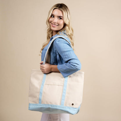 The Signature Canvas Tote Bag, A natural canvas tote bag with black webbing straps, a front pocket, and a gold D-ring, shown against a cream background.