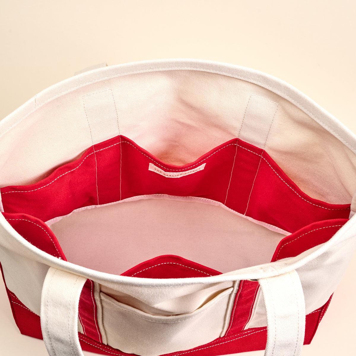The Signature Canvas Tote Bag, A natural canvas tote bag with black webbing straps, a front pocket, and a gold D-ring, shown against a cream background.
