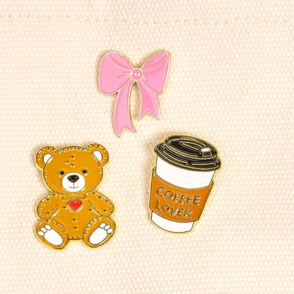 Enamel Pin Pack, A boxed set of three gold enamel pins in the Latte Love design, a coffee cup, a teddy bear, and a pink bow.