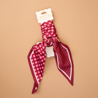 Twirl & Tie Scarf Accessory, A red and white gingham satin scarf tied in a knot, showing a red polka dot pattern on the reverse side of the tails.