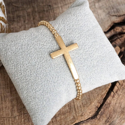 Pulsera elástica minimalista con cruz en tono dorado desgastado y cuentas de bola