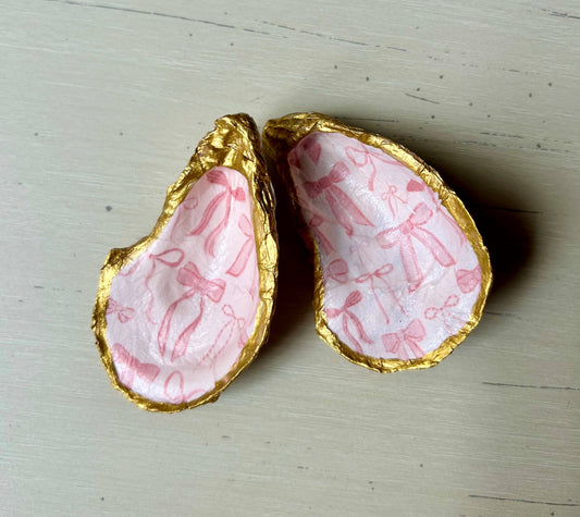 Plato para joyas con forma de concha de ostra y lazo rosa.