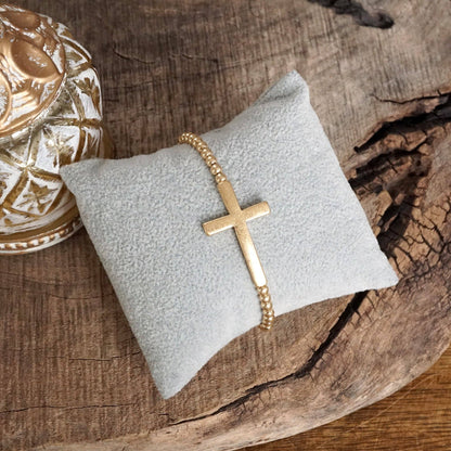 Pulsera elástica minimalista con cruz en tono dorado desgastado y cuentas de bola
