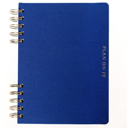 Cobalt Blue Fabric-Bound Task Journal, A cobalt blue fabric-covered task journal with gold twin wire spirals and two navy ribbon bookmark tabs, closed with an elastic band.