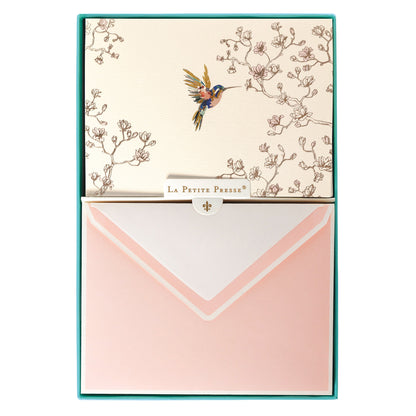 La Petite Presse Hummingbird Boxed Correspondence Notes, A cream notecard with a colorful hummingbird and gold magnolia branch line art, paired with a blush pink lined envelope.