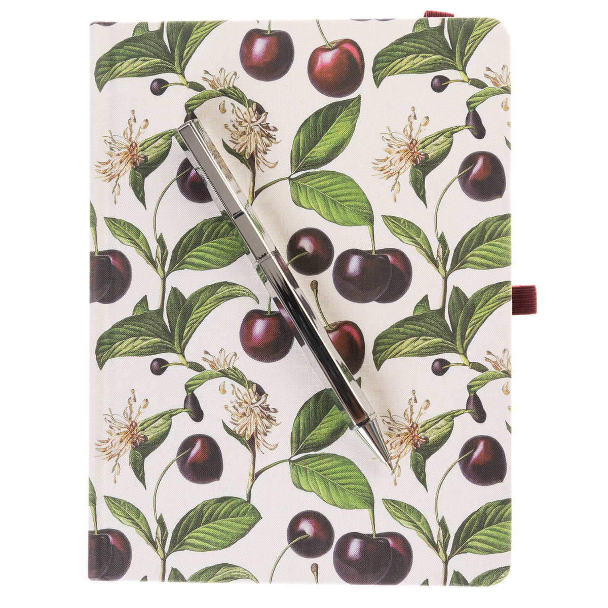 La Petite Presse Cerise Fabric-Bound Journal with Pen, An ivory fabric journal printed with botanical cherries and blossom sprigs, closed with a burgundy elastic band and a silver pen tucked into a loop.