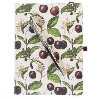La Petite Presse Cerise Fabric-Bound Journal with Pen, An ivory fabric journal printed with botanical cherries and blossom sprigs, closed with a burgundy elastic band and a silver pen tucked into a loop.