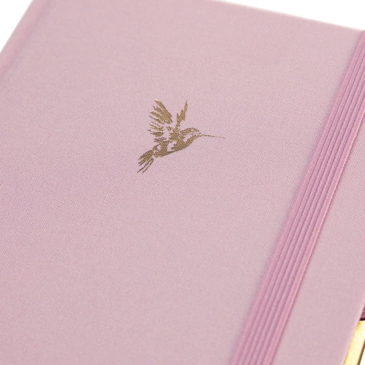 La Petite Presse Hummingbird Fabric-Bound Journal with Pen, A pink fabric journal with a gold foil hummingbird on the cover, paired with a gold twist pen tucked into a loop at the spine.