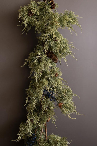 Artificial Juniper Christmas Garland with Berries, A faux juniper garland with red berries and pinecones laid out in a line.
