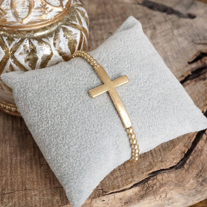 Pulsera elástica minimalista con cruz en tono dorado desgastado y cuentas de bola