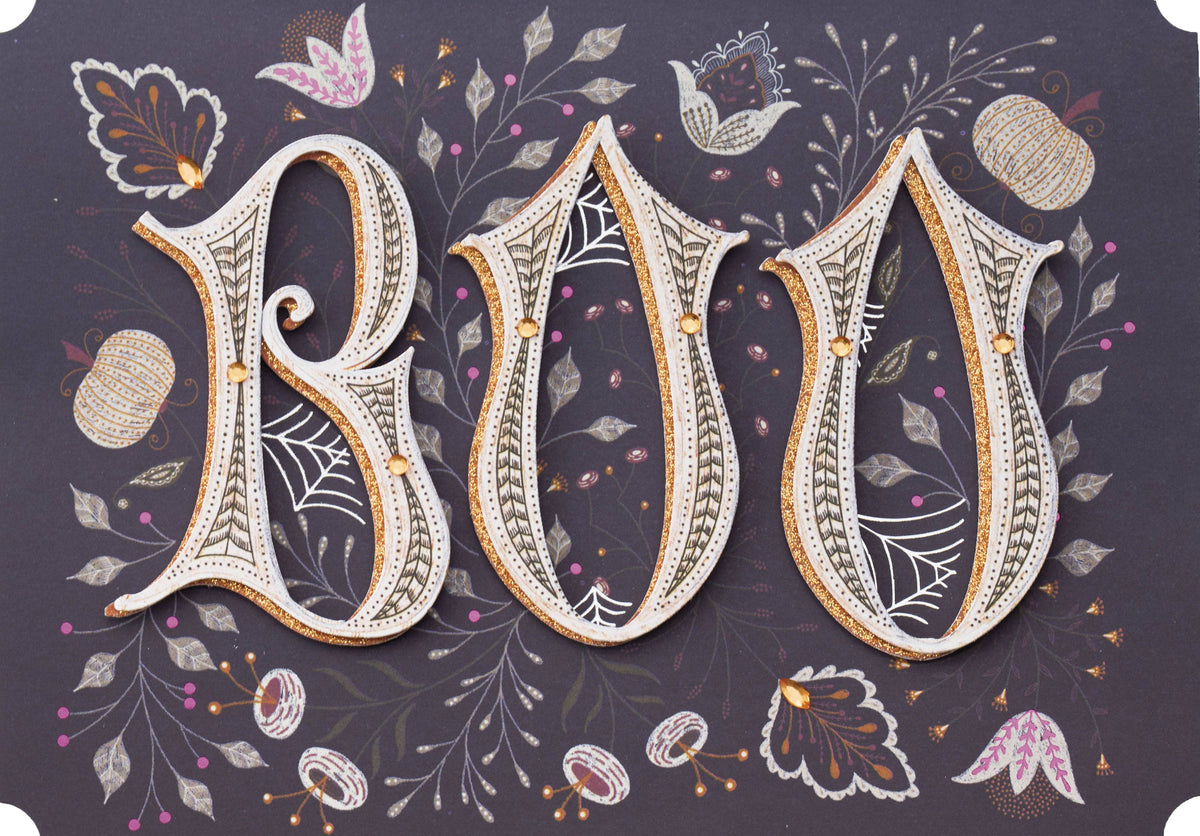 Boo-Jeweled Greeting Card, Front of the card showing the letters BOO in layered cream lettering with a gold glitter edge and small gold gems among drawn leaves, flowers, pumpkins and spiderwebs on a dark plum ground.