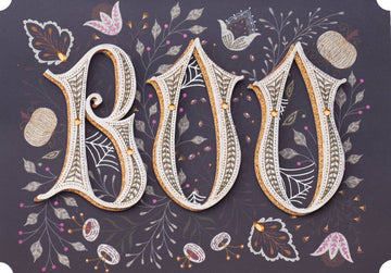 Boo-Jeweled Greeting Card, Front of the card showing the letters BOO in layered cream lettering with a gold glitter edge and small gold gems among drawn leaves, flowers, pumpkins and spiderwebs on a dark plum ground.