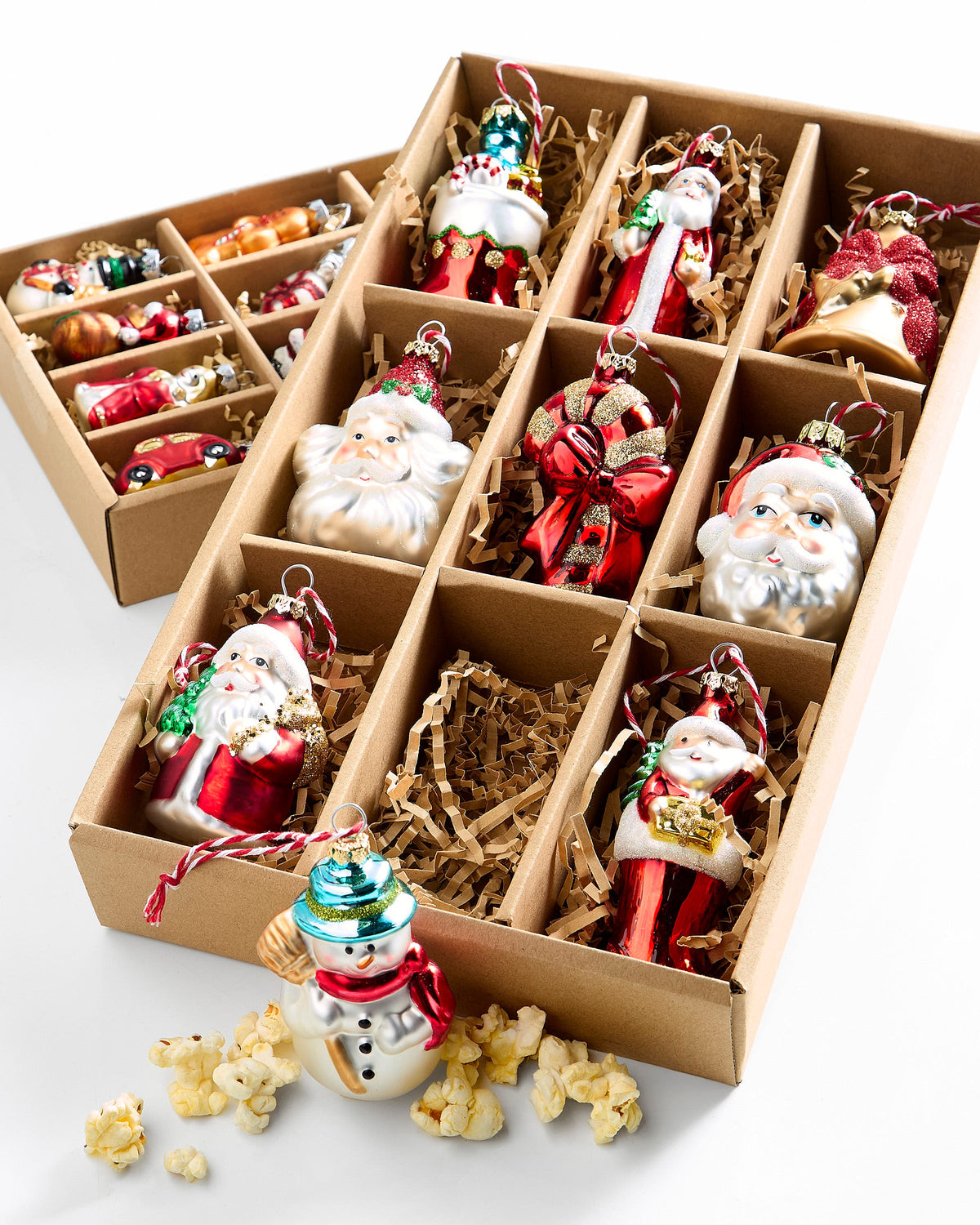 Box of Christmas Ornaments, A cardboard box with nine compartments holding glass Christmas ornaments shaped like Santas, a snowman, a bow and a bell in red, gold, white and green.