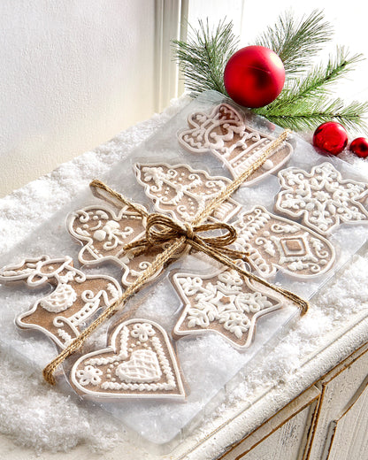 Box of Gingerbread Ornaments, A box of eight flat clay gingerbread-shaped ornaments with white icing detail, tied with twine, including a reindeer, gingerbread man, heart, tree, bell, star, and snowflakes.