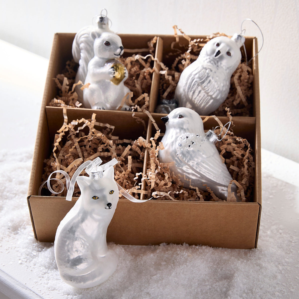 Box of Winter Woodland Animal Ornaments, A box of four pearl white glass ornaments shaped like an owl, a fox, a squirrel and a bird, each with silver or gold accents.