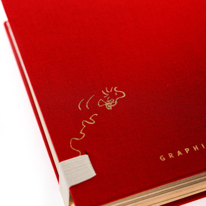 Peanuts Fabric-Bound Notepad, A red fabric-bound notepad with Snoopy typing at his typewriter in gold foil on the cover and gold gilded page edges.