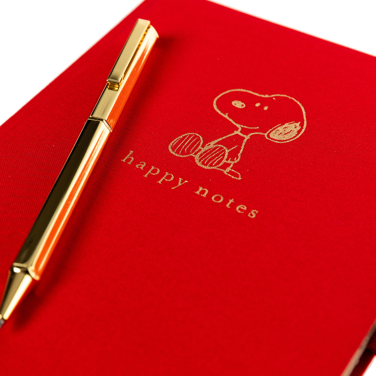 Peanuts Fabric-Bound Journal with Pen, A red fabric journal with a gold foil Snoopy illustration and the words happy notes, paired with a gold pen tucked into a loop along the spine.
