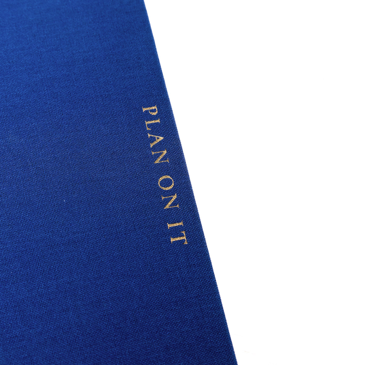 Cobalt Blue Fabric-Bound Task Journal, A cobalt blue fabric-covered task journal with gold twin wire spirals and two navy ribbon bookmark tabs, closed with an elastic band.