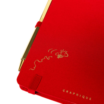 Peanuts Fabric-Bound Journal with Pen, A red fabric journal with a gold foil Snoopy illustration and the words happy notes, paired with a gold pen tucked into a loop along the spine.