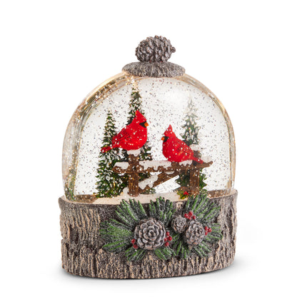 Cardinal Perch Lighted Water Globe, Dome water globe with two red cardinals on a snowy fence among pine trees, set on a bark-look base with pinecones and red berries.