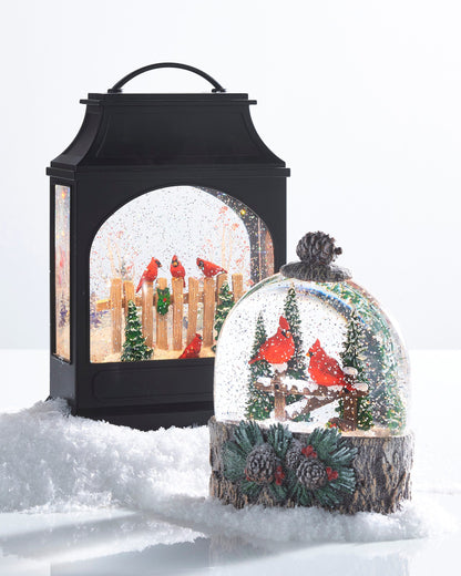 Cardinal Perch Lighted Water Globe, Dome water globe with two red cardinals on a snowy fence among pine trees, set on a bark-look base with pinecones and red berries.