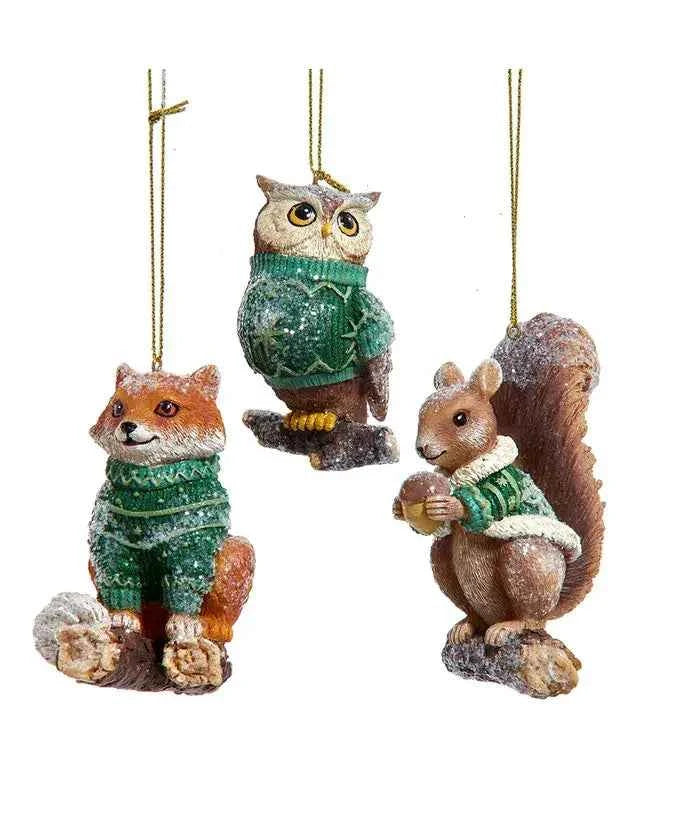 A resin woodland animal ornament in a green knit sweater, dusted with snow glitter.