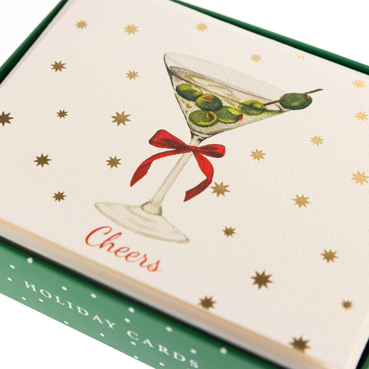 Cheers Holiday Cards, Box of 15, A cream holiday card with a martini glass, green olives and a red bow under gold foil stars and Cheers in red script, set in its green box.