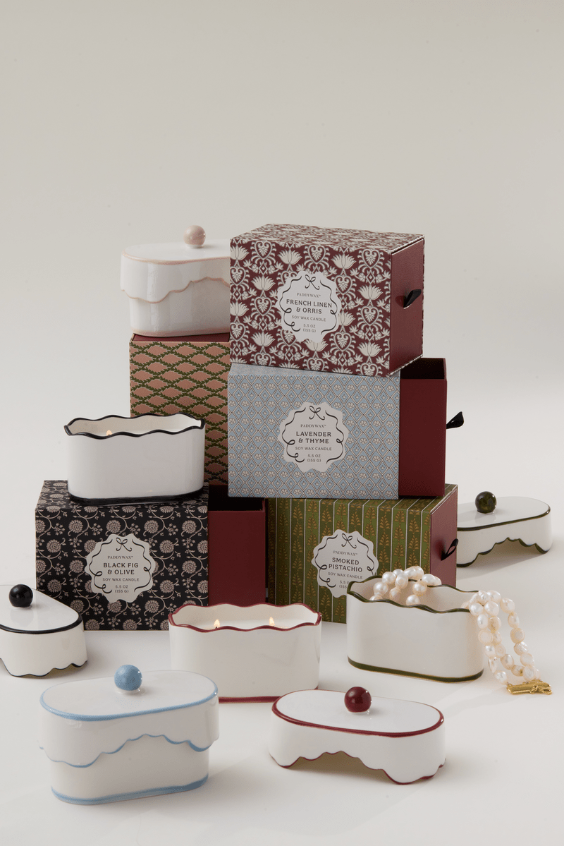 Chérie 5.5 oz Ceramic Candle, A white ceramic lidded candle box with a black scalloped rim and a round knob, tagged Black Fig and Olive.