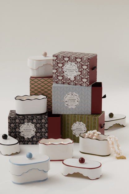 Chérie 5.5 oz Ceramic Candle, A white ceramic lidded candle box with a black scalloped rim and a round knob, tagged Black Fig and Olive.