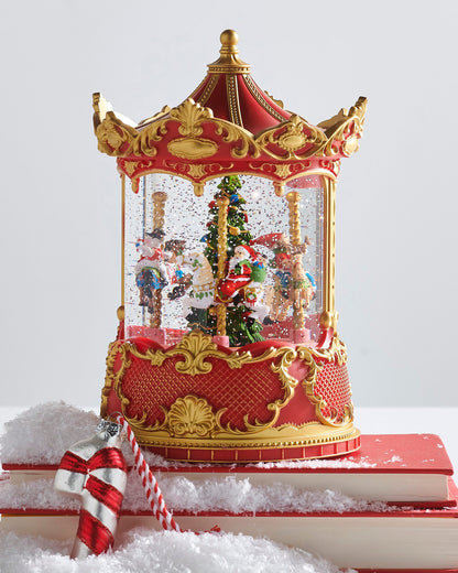 Christmas Carousel Animated Water Globe with Santa and Reindeer, A red and gold carousel-shaped water globe with a rotating base showing Santa, a reindeer, and carousel horses circling a lit Christmas tree amid swirling glitter.