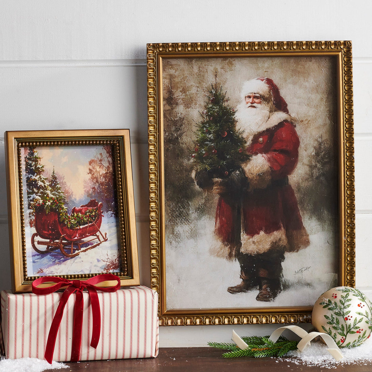 Christmas Sleigh Wall Art, A framed print of a red vintage sleigh loaded with a Christmas tree in a snowy woodland, in a gold beaded frame.