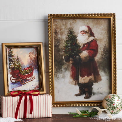 Christmas Sleigh Wall Art, A framed print of a red vintage sleigh loaded with a Christmas tree in a snowy woodland, in a gold beaded frame.