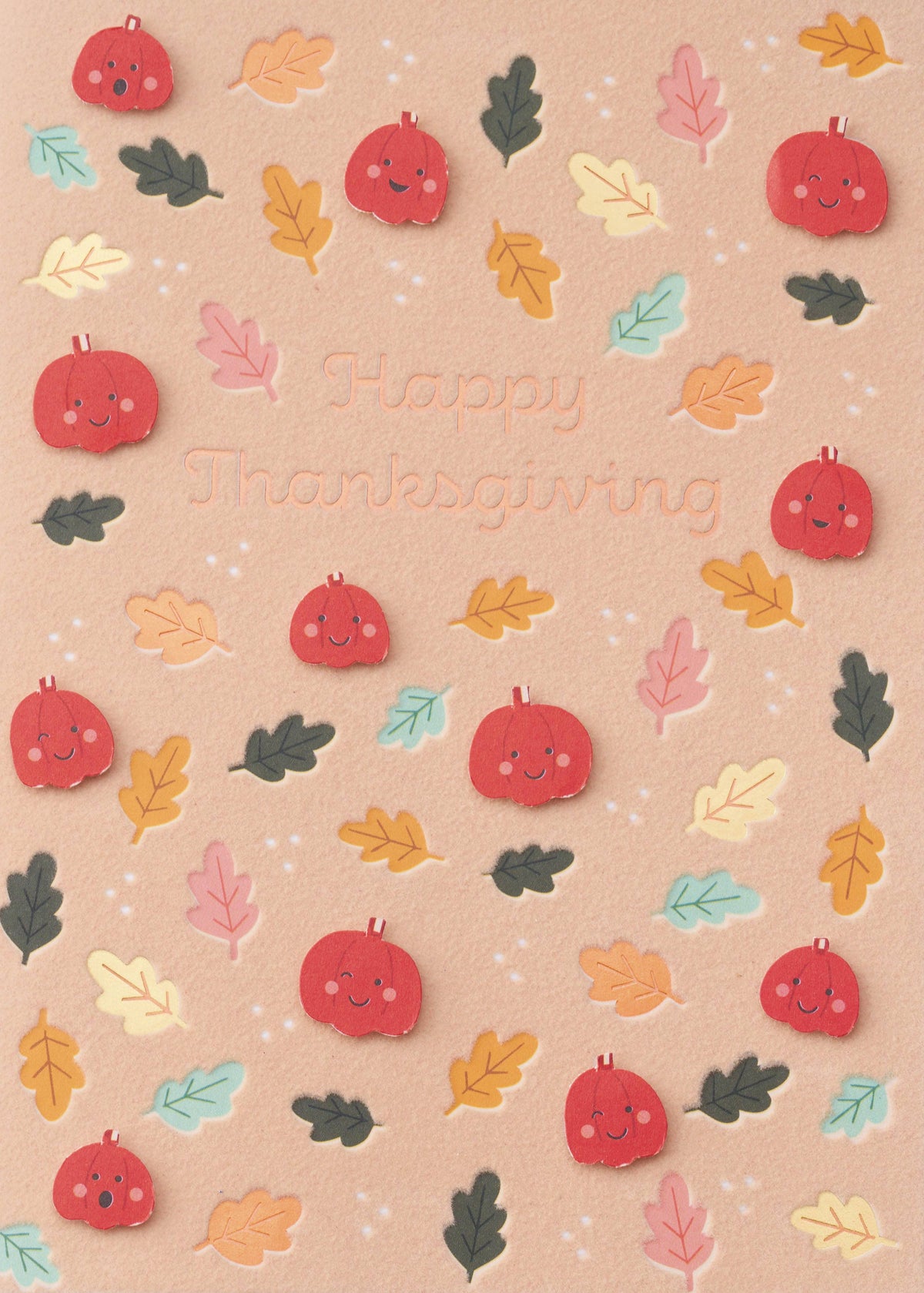 Colorful Autumn Magic Greeting Card, A peach card front scattered with smiling red pumpkin faces and mustard, mint, pink and olive leaves around the words Happy Thanksgiving in script.