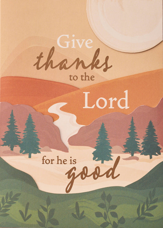 Divine Gratitude Greeting Card, A card front with a landscape of stacked peach, orange and rose hills, evergreen trees, a winding pale river and a round cream sun, with the words Give thanks to the Lord for he is good in brown script and cream lettering.