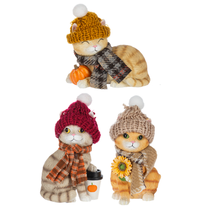 Dressed Up Fall Cat Figurine, Three tabby cat figurines in pom-pom knit hats and scarves, one sleeping beside a pumpkin, one holding a pumpkin coffee cup and one holding a sunflower.