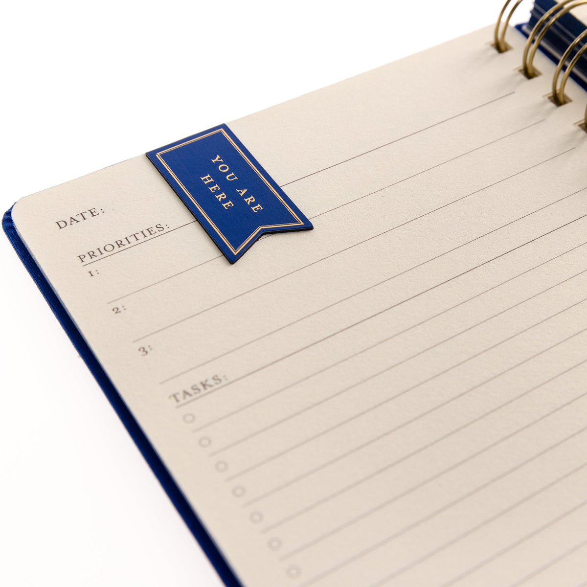 Cobalt Blue Fabric-Bound Task Journal, A cobalt blue fabric-covered task journal with gold twin wire spirals and two navy ribbon bookmark tabs, closed with an elastic band.