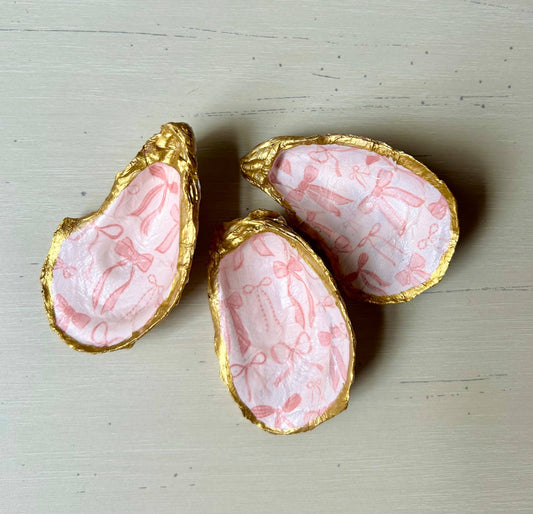 Plato para joyas con forma de concha de ostra y lazo rosa.