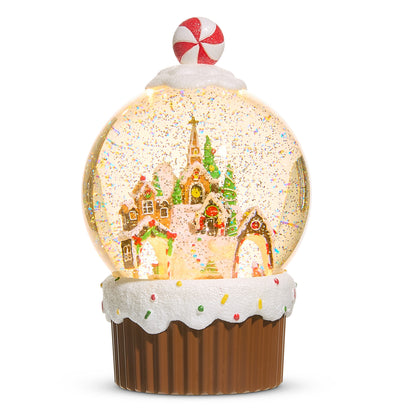 Gingerbread Village Cupcake Lighted Water Globe, A lighted snow globe holding a gingerbread village with evergreens and a church spire, set in a frosted cupcake base with sprinkles and a peppermint candy on top of the dome.