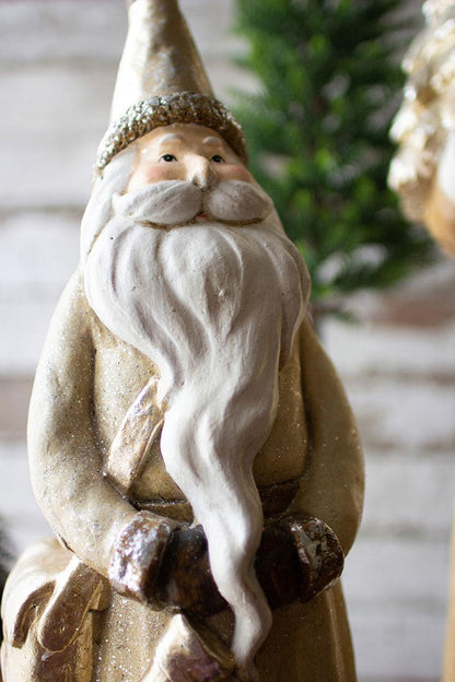 Gold Resin Santa, Two resin Santa figures in muted gold cloaks, the taller holding a small Christmas tree and the shorter holding a stocking.