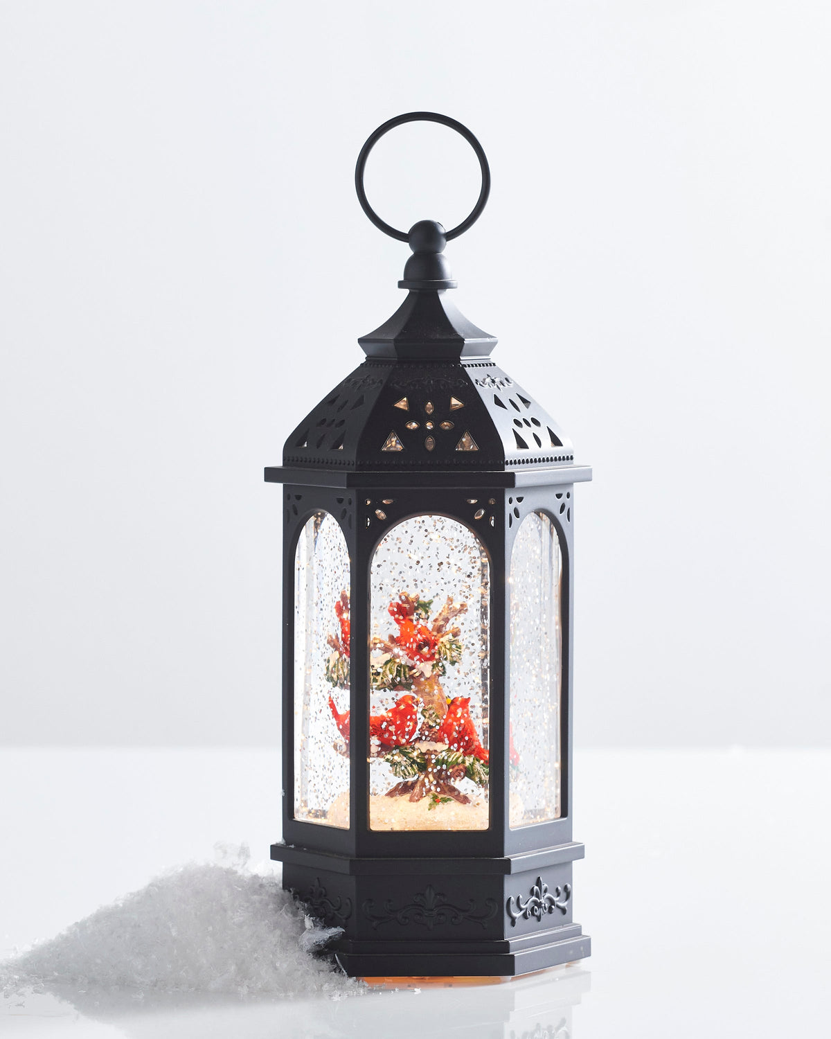 Hexagonal Cardinal Tree Lighted Water Lantern, A six-sided black water lantern with a pierced roof and ring handle, showing several red cardinals perched in a snowy tree behind glitter-filled arched windows.