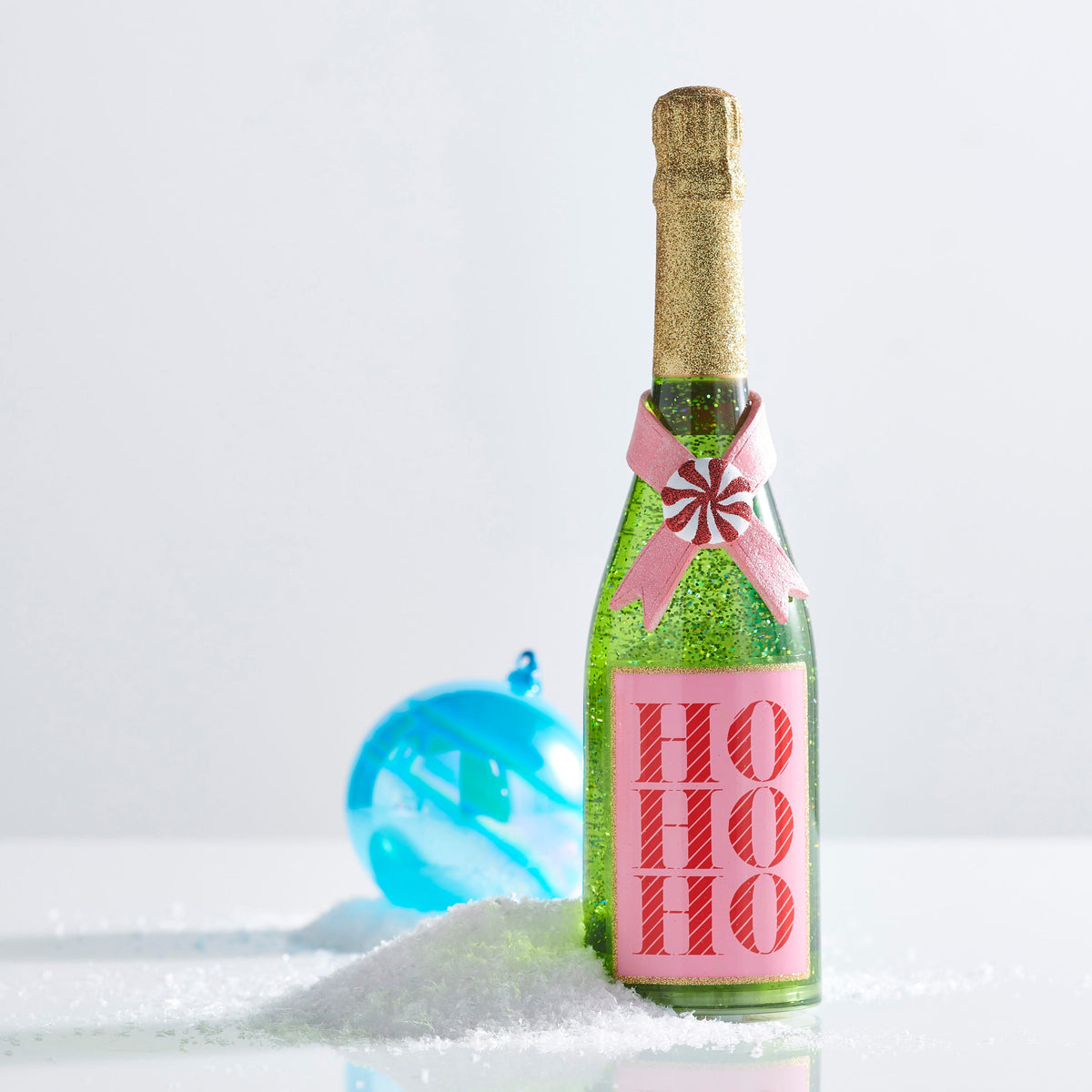 Ho Ho Ho Pink and Green Lighted Glitter Bottle, A green lighted bottle filled with green glitter, with a neck coated in gold glitter, a pink ribbon crossed under a peppermint candy, and a pink label printed with HO HO HO in red striped letters.