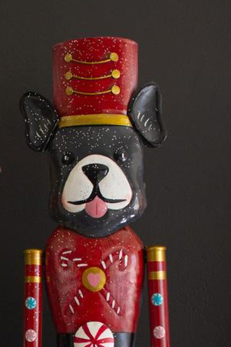 Painted Metal Dog Nutcracker, Black and White Dog design: a close view of the black and white dog head with upright black ears under a red shako hat, above a red tunic with a candy cane.