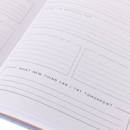 Manifest Self-Care Journal, A periwinkle blue fabric journal printed with celestial suns, moons, and stars under 'Manifest Your Dreams' in gold foil.