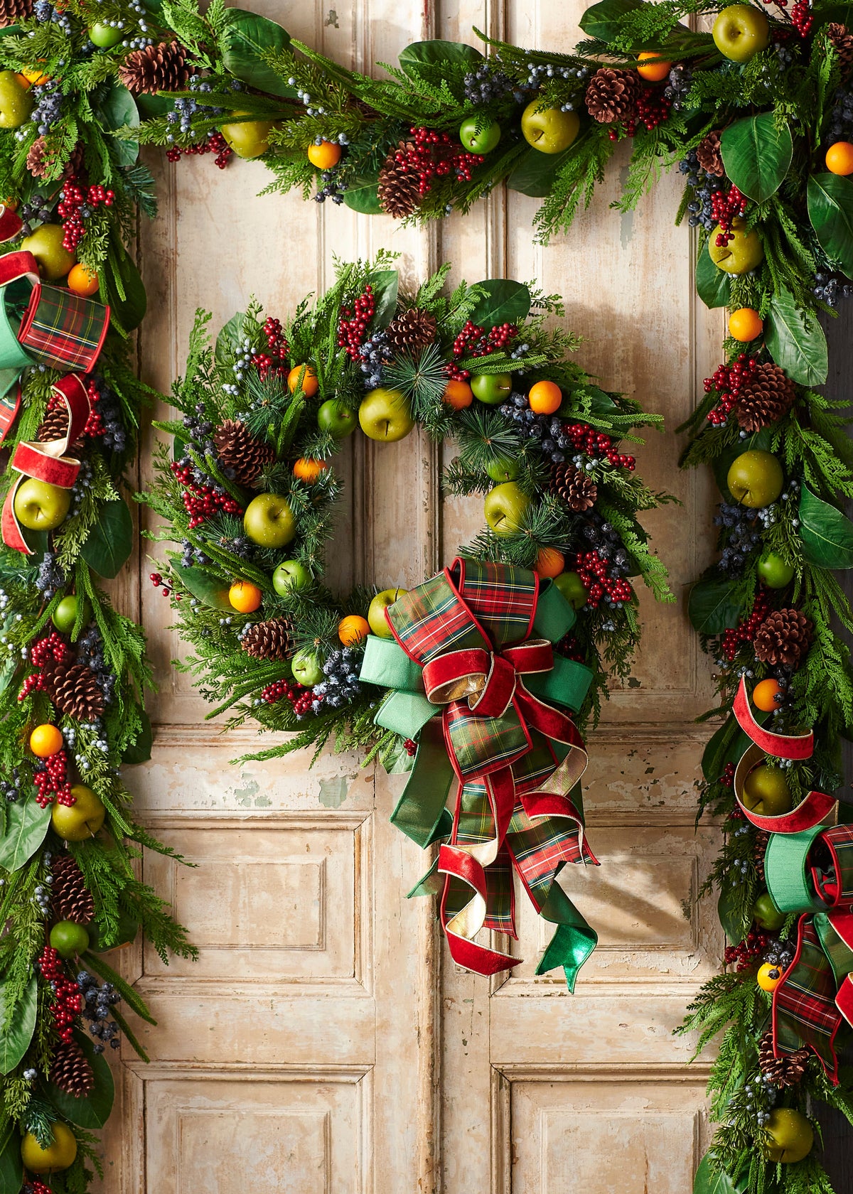 Mixed Fruit Wreath, The photo shows a round wreath of mixed greenery, pinecones, red berries, and faux green apples and oranges.