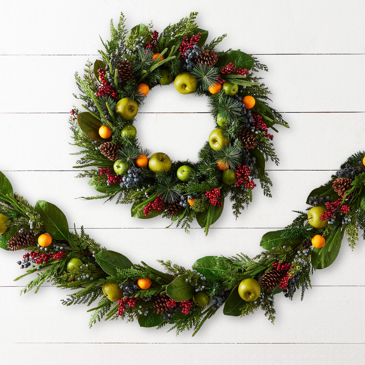 Mixed Fruit Wreath, The photo shows a round wreath of mixed greenery, pinecones, red berries, and faux green apples and oranges.