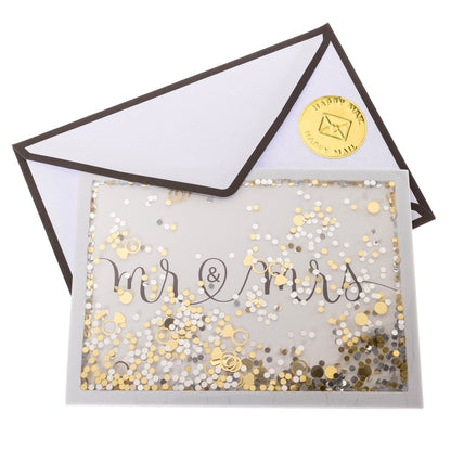 Mr. and Mrs. Wedding Handmade Card, A white card reading mr & mrs in black script behind a gold and silver confetti shaker with gold ring shapes, shown with its envelope.