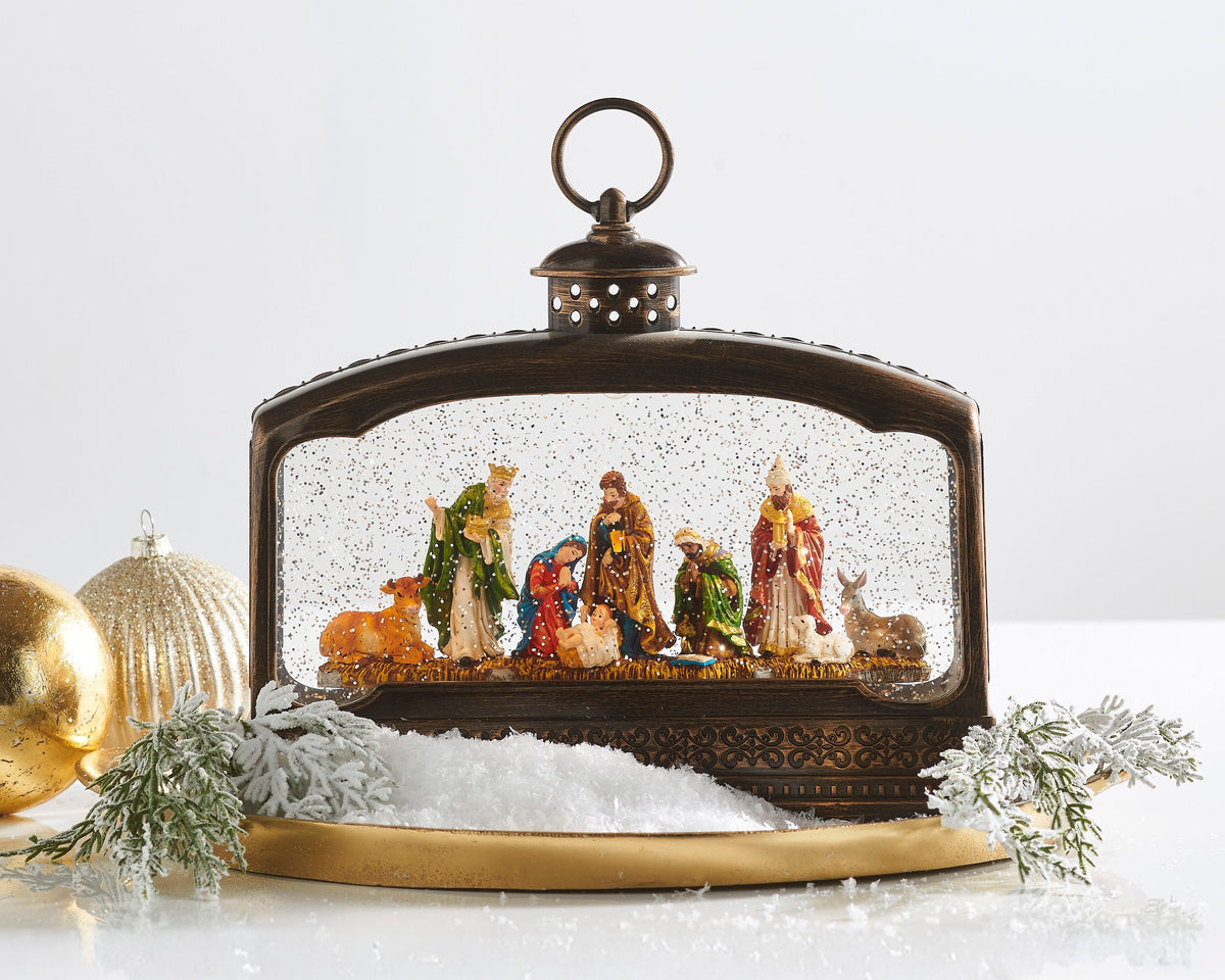 Nativity Lighted Water Terrarium, A wide bronze-finish lantern with a ring handle showing a nativity scene of Mary, Joseph, the infant in the manger, three kings, an ox, a donkey and a lamb amid swirling glitter.