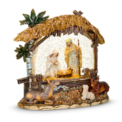 Nativity Stable Lighted Water Lantern, A resin nativity stable with a thatched roof and palms, Mary and Joseph at the manger behind glittered water, and a donkey, a lamb and an ox resting on the base.