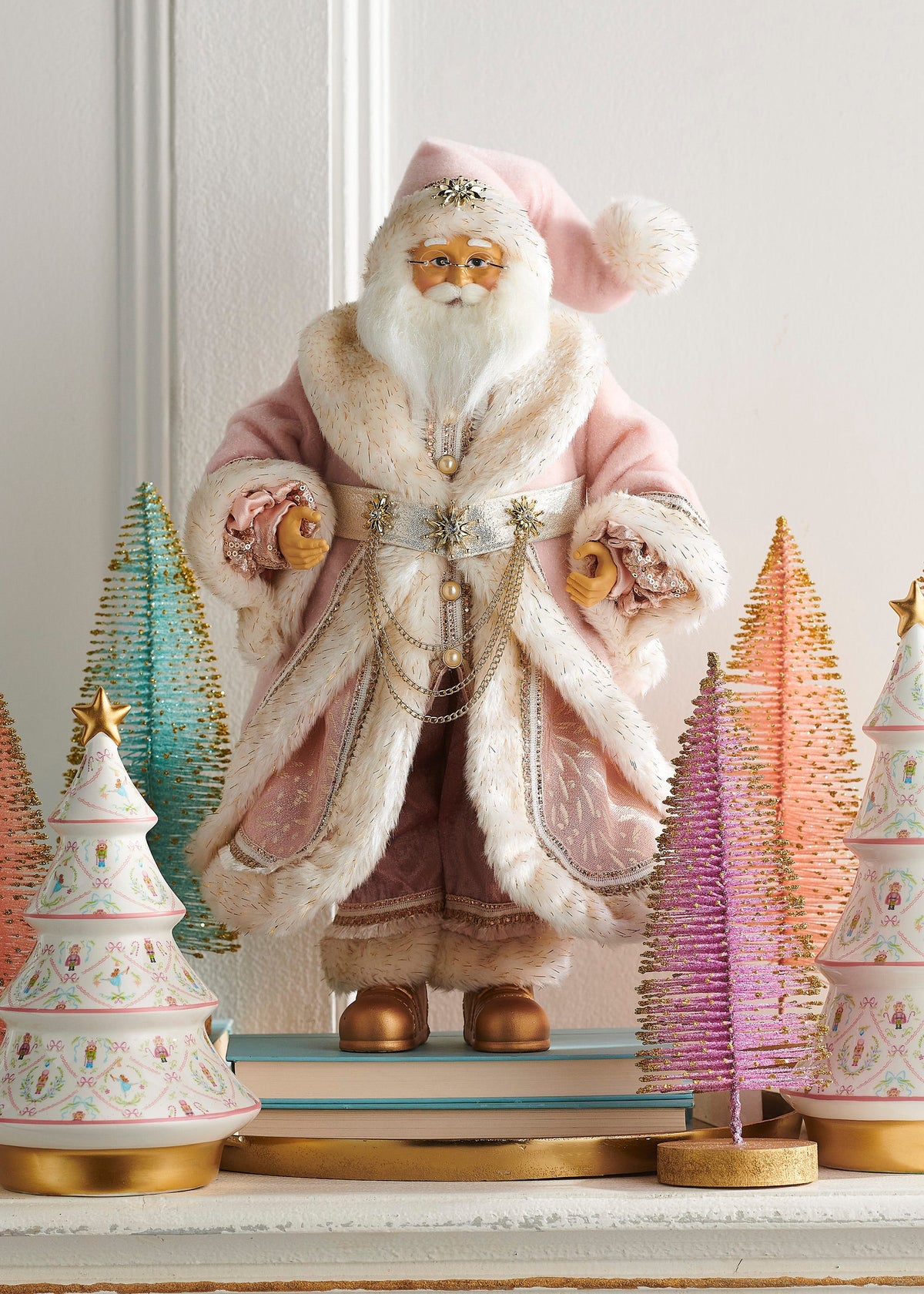 Nutcracker Suite Santa Figure in Light Pink, A standing Santa figure in a light pink coat and cap trimmed in ivory plush, with wire-rimmed glasses, gold chain swags at the waist and gold boots.